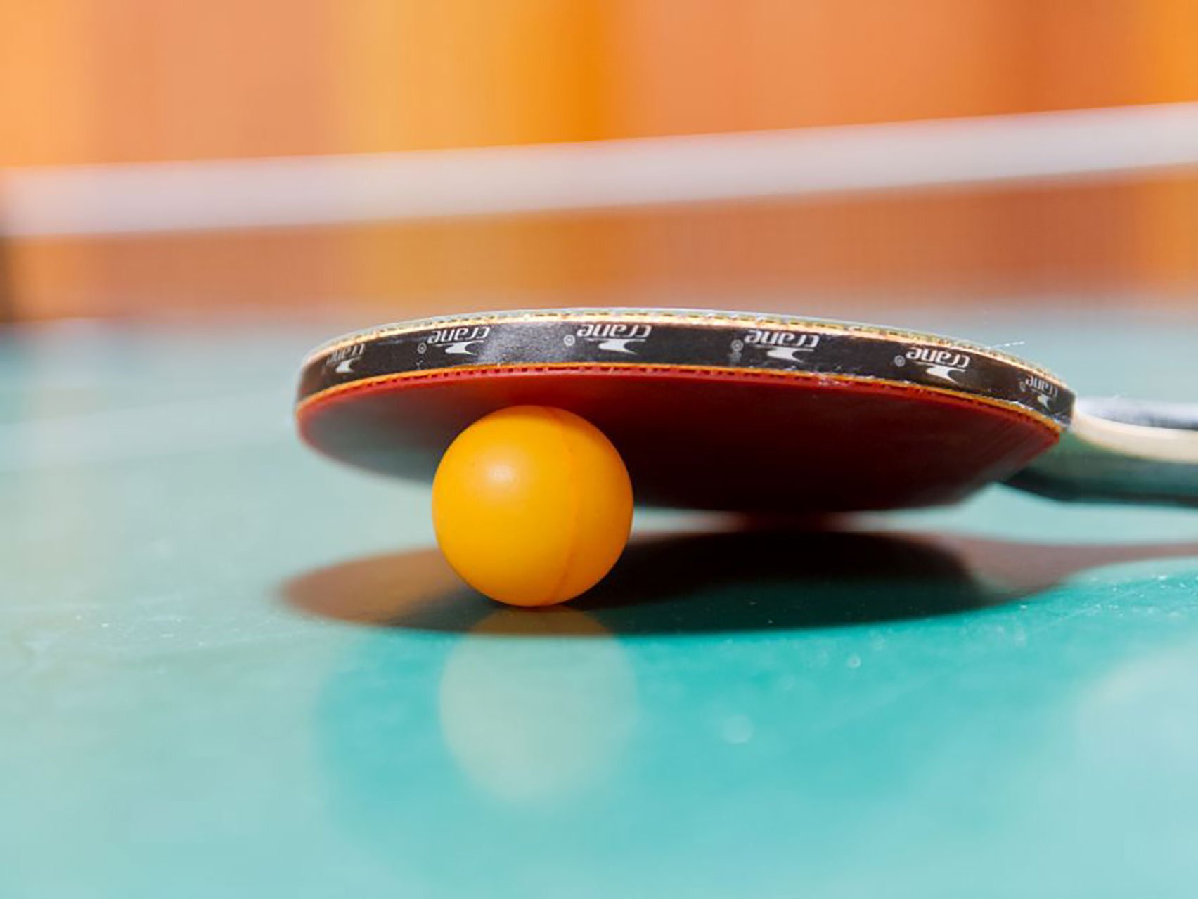 Nahaufnahme: gelber Tischtennisball unter einem roten Tischtennisschläger