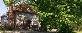 Aussenansicht auf Haus Klein Linde - im Vordergrund steht ein altes Kutsch-Rad auf einer Wiese