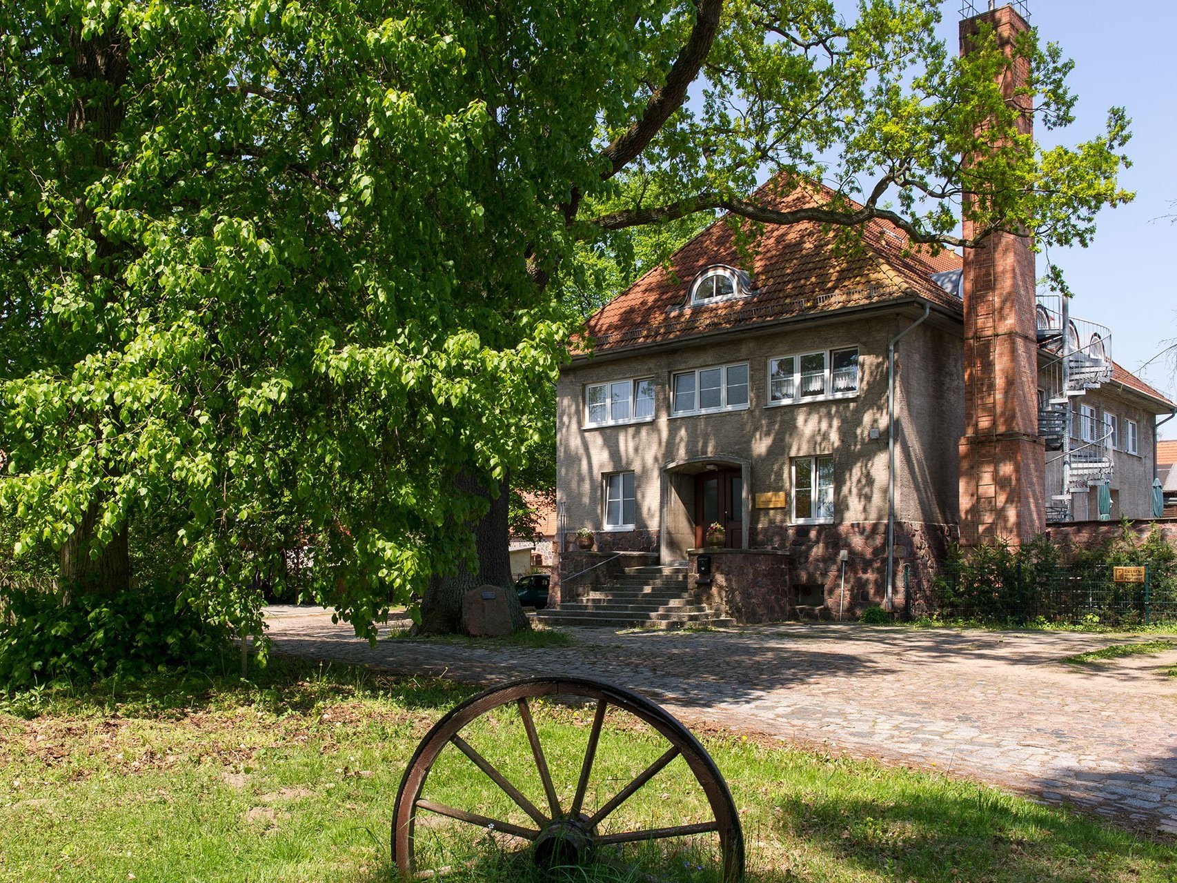 Aussenansicht auf Haus Klein Linde - im Vordergrund steht ein altes Kutsch-Rad auf einer Wiese