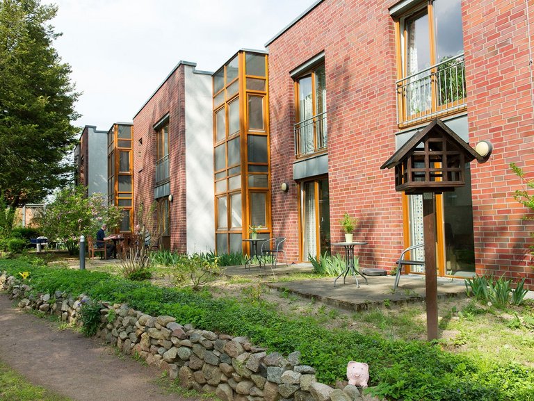 Backsteinhausfassade mit mehreren Terassen - im Hintergrund zwei Männer an einem Gartentisch